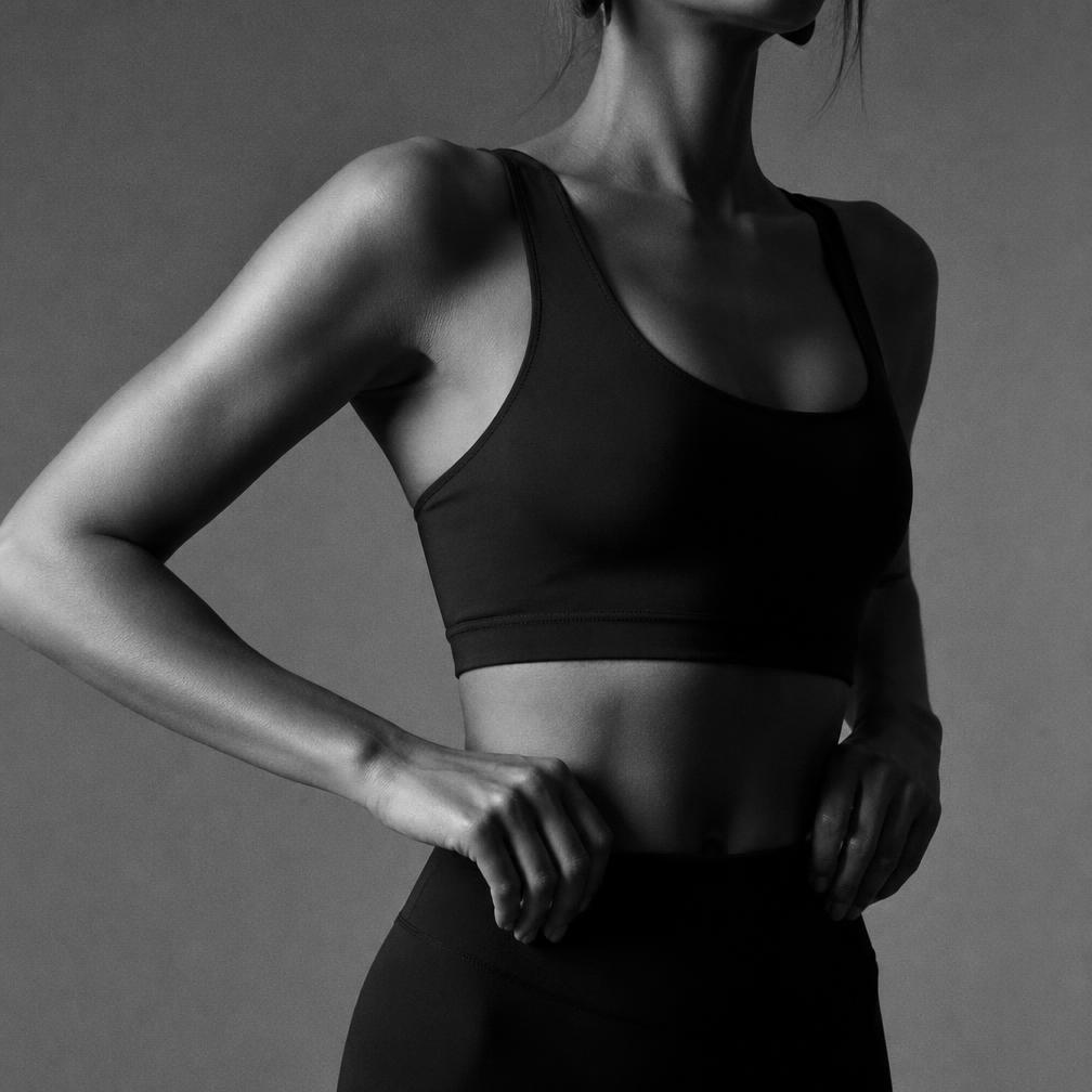 Studio portrait of a woman standing in plain black activewear, shoulder to hip